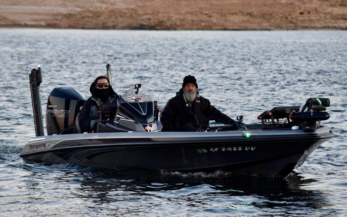Two people on a bass boat in a body of water with a scenic background